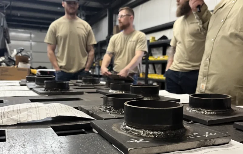 Judges scoring pipe-on-plate test coupons at the 2025 HWA Welding Competition